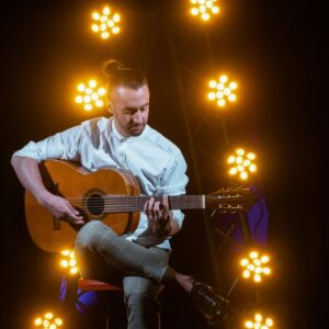 A person playing a guitar on stage, surrounded by glowing lights.
