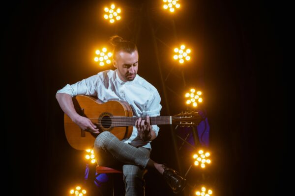 A person playing a guitar on stage, surrounded by glowing lights.