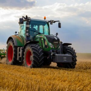 A person drives a green tractor plowing a field under a cloudy sky.