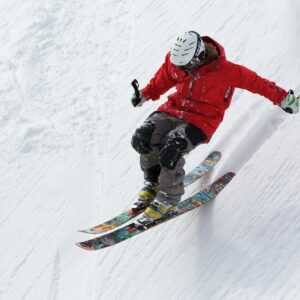 A person in a red jacket skiing downhill on a snowy slope, showcasing vibrant skis.