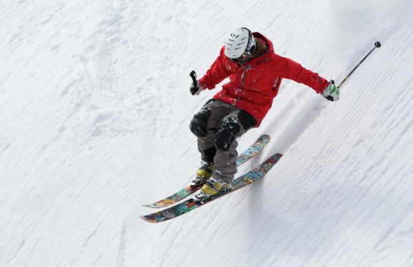 A person in a red jacket skiing downhill on a snowy slope, showcasing vibrant skis.
