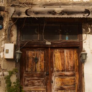 Weathered wooden door set in a crumbling plaster wall, with vintage lamps and ivy growing nearby.