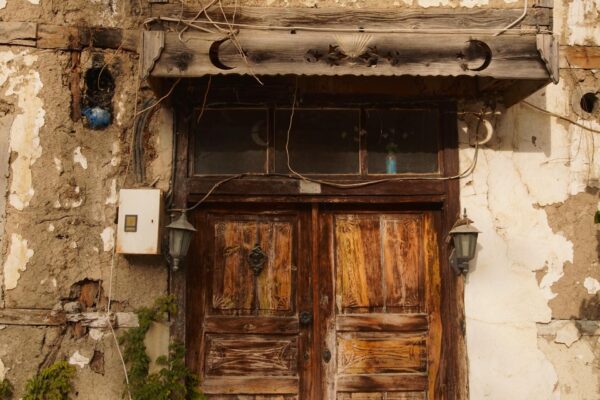 Weathered wooden door set in a crumbling plaster wall, with vintage lamps and ivy growing nearby.