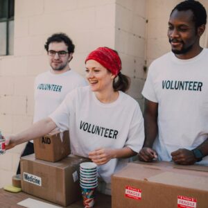 Volunteers distributing supplies, smiling and organizing boxes labeled aid and medicine on a table outdoors.