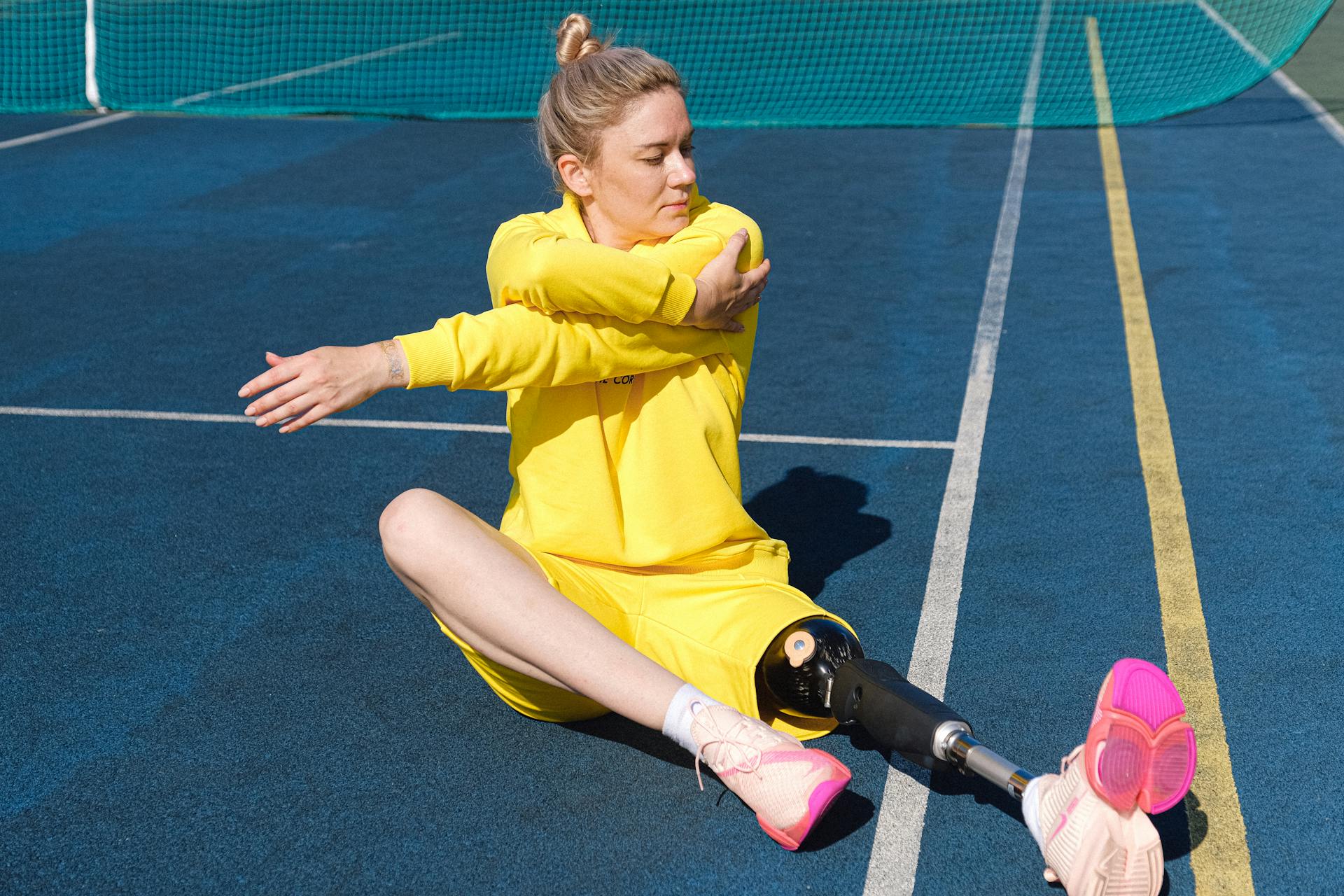 A person in a yellow outfit stretches on a track, showcasing resilience and athleticism.